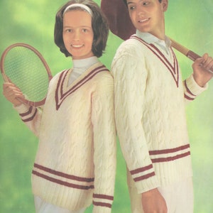 May include: Two white cable knit sweaters with red and white stripes. The sweaters have a v-neck and are worn by two people holding tennis rackets.