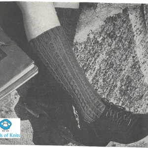 Könnte beinhalten: Nahaufnahme eines Beins, das graue Stricksocken mit einem Zopfmuster trägt. Die Socken werden mit schwarzen Schuhen getragen. Das Bild ist in Schwarzweiß.
