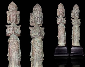 Op de afbeelding: Vier antieke bronzen beelden van figuren in traditionele kleding met uitgebreide hoofdtooien. De figuren staan met hun handen gevouwen in gebed. De beelden staan op zwarte sokkels.