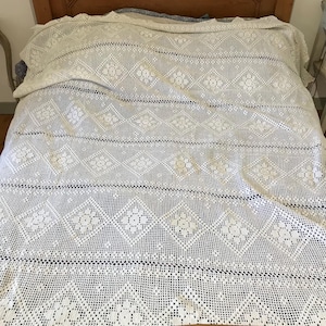 Puede incluir: Colcha de cama blanca de ganchillo con un patrón de diamante y detalles florales.