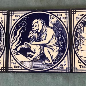May include: Three blue and white ceramic tiles with illustrations of animals. The first tile shows a fox and a stork, the second tile shows a monkey holding a cat, and the third tile shows a fox and a dog. The tiles have text in a blue font.