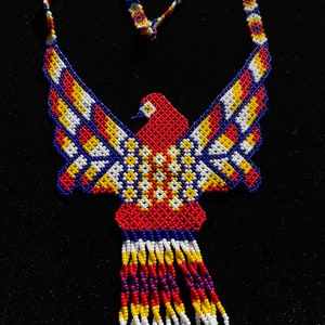 Peut inclure: Un collier de perles avec un motif d'oiseau rouge, jaune, bleu et blanc. Le collier est fait de petites perles colorées et a une frange en bas.