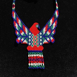 Peut inclure: Un collier de perles avec un motif d'oiseau rouge, blanc, bleu et vert. L'oiseau a une longue queue avec une frange de perles.
