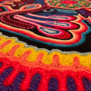 May include: Close-up of a colourful embroidered textile with a circular design. The design features a variety of colours, including red, blue, yellow, green, and white. The textile is made of a soft, textured fabric.