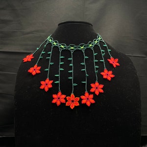 May include: A beaded necklace with red flowers and green leaves. The necklace is made of small beads and is strung together in a delicate pattern. The flowers are arranged in a cascading design, and the leaves are interspersed throughout the necklace.