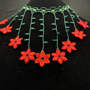 May include: A beaded necklace with a cascading design of orange and red flowers with green leaves. The necklace is made of small beads and has a delicate, feminine look.