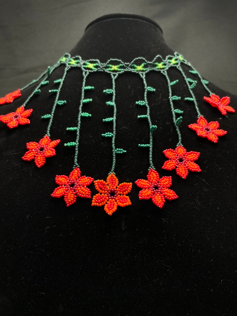 May include: A beaded necklace with a cascading design of orange and red flowers with green leaves. The necklace is made of small beads and has a delicate, feminine look.