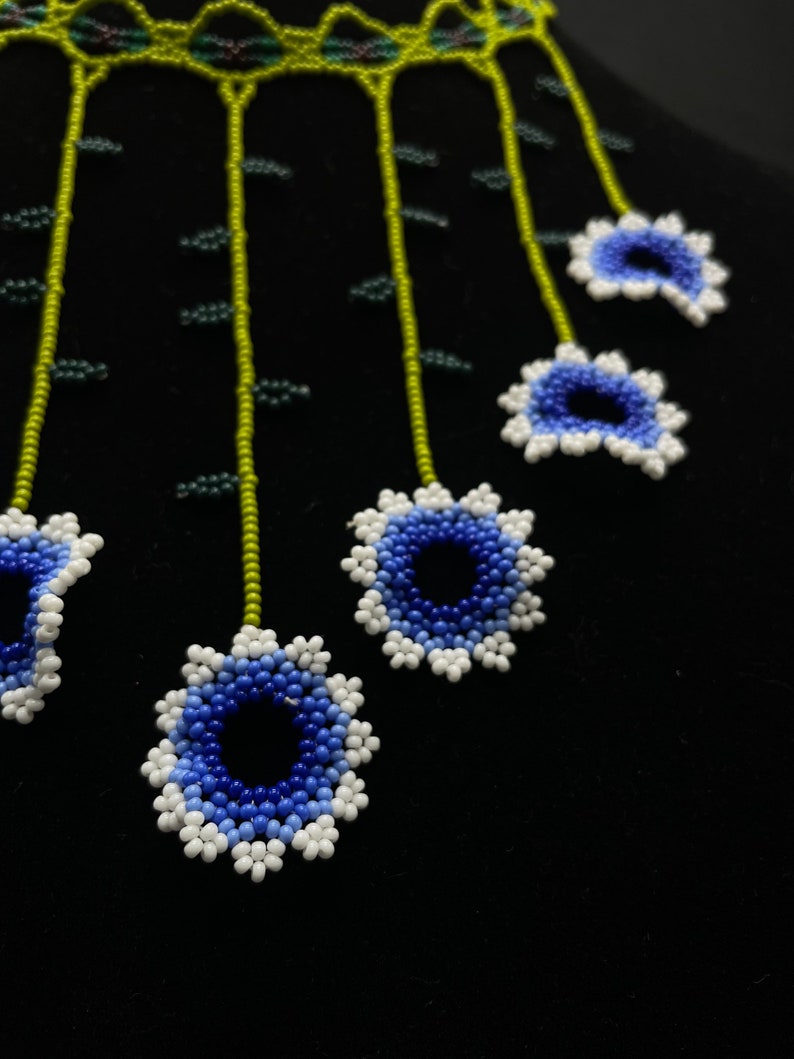 May include: A beaded necklace with a green and white base and blue and white flower accents.
