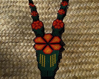 May include: A long beaded necklace with a green, orange, and black floral design. The necklace has a tassel at the bottom.