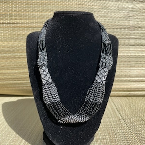 May include: A multi-strand necklace made of black and silver beads. The necklace is displayed on a black velvet bust form.