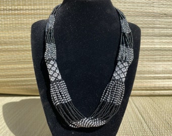 May include: A multi-strand necklace made of black and silver beads. The necklace is displayed on a black velvet bust form.