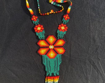 May include: A beaded necklace with a large orange flower pendant and a green tassel. The necklace is made of small, colorful beads and has a traditional Mexican design.