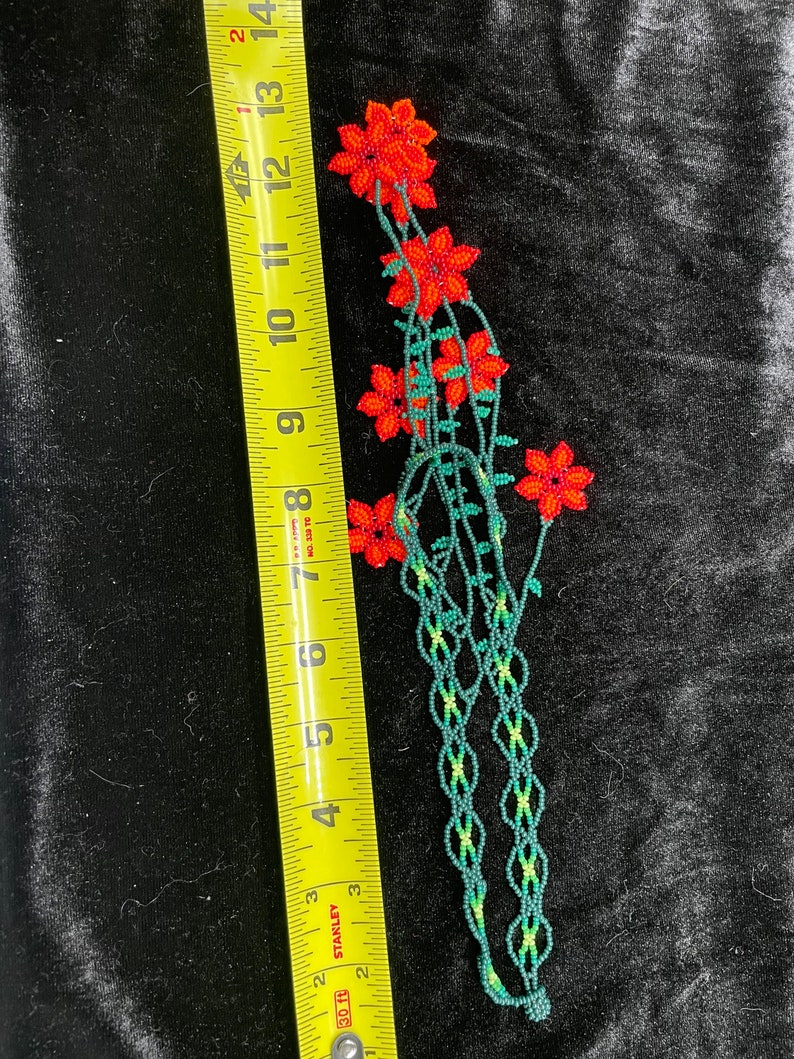 May include: A beaded flower garland with red flowers and green leaves. The garland is approximately 12 inches long.