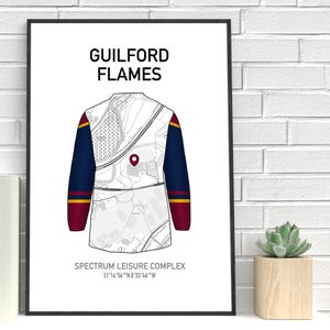 May include: A framed print featuring a stylized illustration of a Guilford Flames jersey. The jersey design incorporates a map-like pattern with navy blue sleeves, accented with red and gold stripes. Text at the top reads "GUILFORD FLAMES".