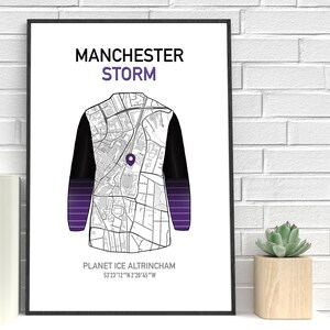 May include: A framed print featuring a map design in the shape of a jacket, with the text "MANCHESTER STORM" at the top. The jacket design has black sleeves and a purple gradient at the bottom. The text "PLANET ICE ALTRINCHAM" is at the bottom.
