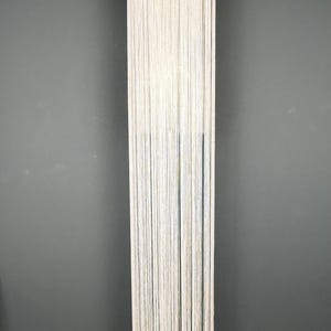 May include: A floor-length halter-style garment made entirely of long, thin, off-white fringe strands. The piece features a high neckline that secures around the neck, with the fringe cascading down in a straight, uniform vertical line.