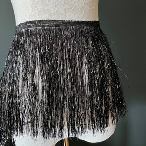 May include: Black fringe trim with silver glitter. The fringe is approximately 7.5 cm long.