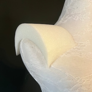 Pode incluir: Forma de busto de espuma branca com uma sobreposição de renda. A forma de busto é projetada para exibir roupas e acessórios.