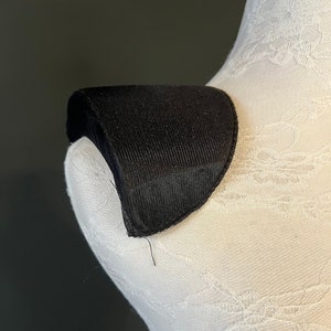 May include: Black fabric collar with a curved shape, designed to be worn on the shoulder.