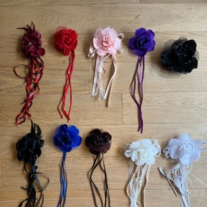 May include: Assortment of ten fabric flower hair clips in various colours and styles. The flowers are made of fabric and have a variety of textures. The clips are attached to long ribbons.