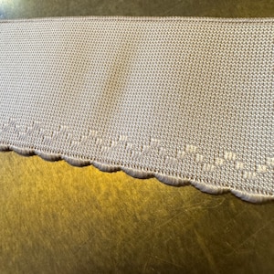 Pode incluir: Um close-up de uma guarnição branca festoneada com um padrão delicado de pontos. A guarnição é feita de um material macio e flexível e é perfeita para adicionar um toque de elegância a qualquer projeto.