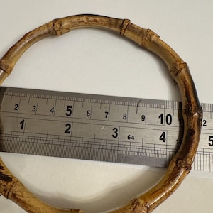 May include: A natural bamboo bangle bracelet. The bracelet is measured with a ruler, showing a diameter of approximately 4 inches. The bamboo has a light brown color with darker brown accents, and the natural joints are visible.