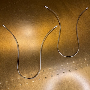 Op de afbeelding: Drie zilveren draad haarbandjes met witte uiteinden. De haarbandjes liggen op een gouden oppervlak.