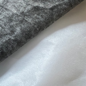 Puede incluir: Primer plano de dos muestras de tela. Una es una tela gris oscura texturizada, la otra es una tela blanca lisa.
