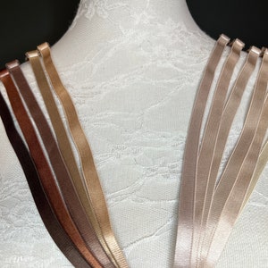 Può includere: Assortimento di spalline per reggiseno in varie tonalità di marrone e beige. Le spalline sono realizzate in un materiale morbido e setoso e sono progettate per essere regolabili.