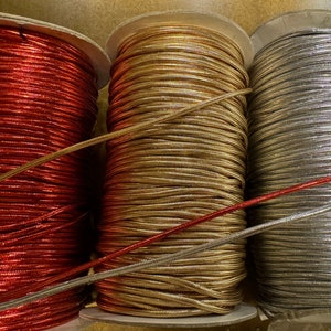 May include: Three spools of metallic cord, one red, one gold, and one silver. The cords are wound tightly on the spools.