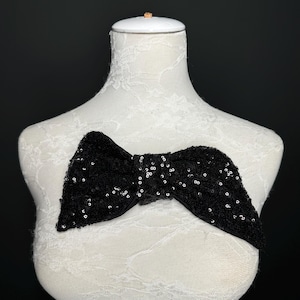 May include: A black sequined bow tie on a white lace-covered mannequin.