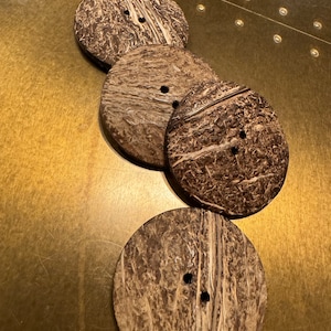 Op de afbeelding: Vier bruine kokosnootknopen, elk met twee gaten. De knopen zijn gestapeld, met de grootste knop onderaan en de kleinste knop bovenaan.