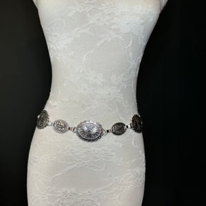 May include: A silver chain belt with oval-shaped charms. Each charm has a detailed design.