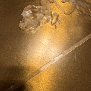 May include: A close-up of a gold surface with a clear plastic tape strip and a pile of clear plastic tape. The surface has a textured pattern and several small, round, gold metal accents.