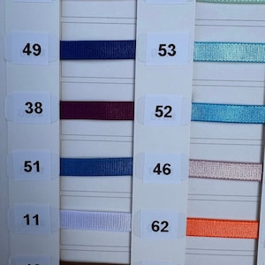 Puede incluir: Una carta de colores con muestras de cintas de diferentes colores. Los colores de las cintas incluyen: rosa claro, azul marino, burdeos, azul, rosa claro, naranja, marrón y morado. Los números 66, 49, 38, 51, 11, 13, 27, 53, 52, 46, 62 y 35 están impresos en la carta.