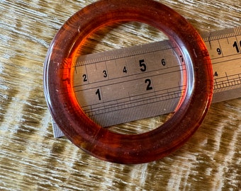 May include: A large, round, amber-colored plastic ring measuring approximately 5 inches in diameter. The ring is lying on a wooden surface.