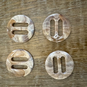 Puede incluir: Cuatro hebillas redondas de plástico marmoleado blanco y marrón con dos ranuras recortadas.