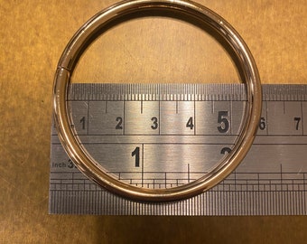 May include: A gold-colored metal ring with a diameter of 1.5 inches, measured against a ruler.