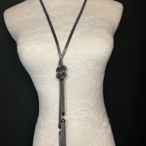May include: A long black chain necklace with a knotted design and tassel accents.