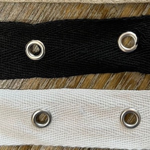 May include: Two strips of fabric with metal eyelets. The top strip is black and the bottom strip is white.