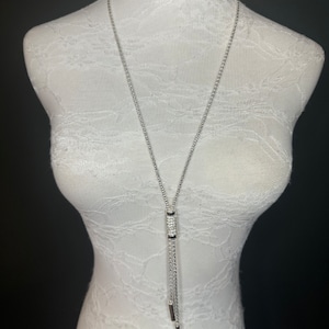 May include: A silver chain necklace with a crystal-encrusted pendant and two dangling silver bars.