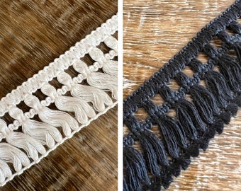 May include: Two samples of fringe trim, one white and one black. Both trims have a repeating pattern of small loops and tassels.