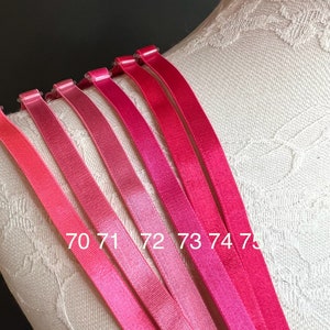 Może przedstawiać: Siedem różowych ramiączek do biustonosza w różnych odcieniach różu, ponumerowanych od 70 do 75.