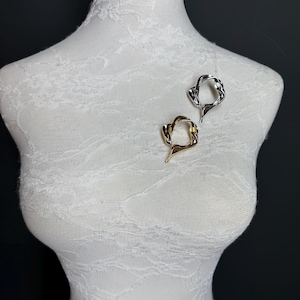 May include: Two abstract metal rings, one gold and one silver, are displayed on a white mannequin. The rings are both open and have a unique, organic shape.