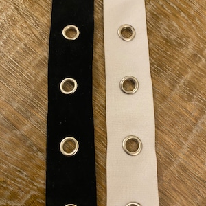 May include: Two strips of fabric with silver eyelets. One strip is black velvet and the other is white.