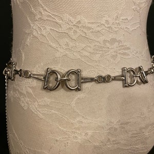 May include: A silver chain belt with a repeating pattern of interlocking 'O' shapes. The belt has a 'BABA' design in the center.