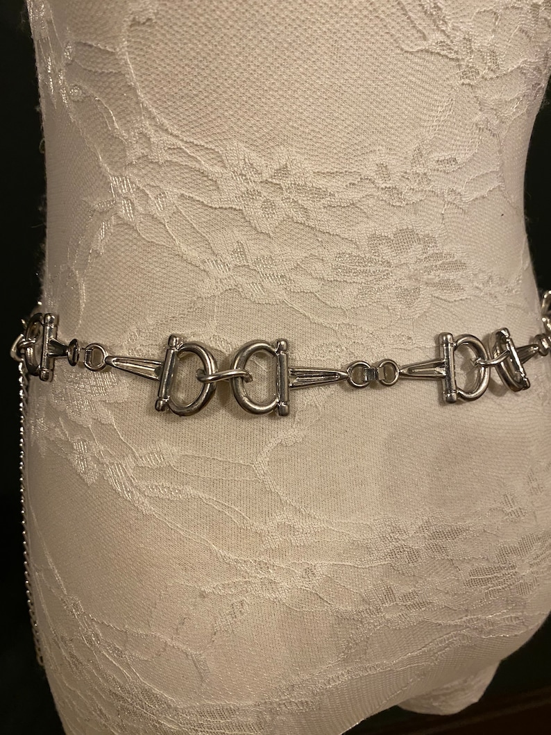 May include: A silver chain belt with a repeating pattern of interlocking 'O' shapes. The belt has a 'BABA' design in the center.