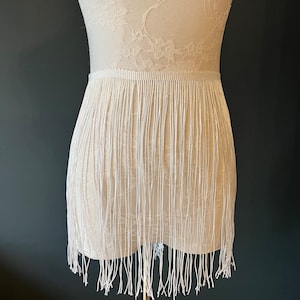 May include: White fringe trim with a delicate lace pattern. The fringe is approximately 7.6 cm long and is perfect for adding a touch of elegance to any project.