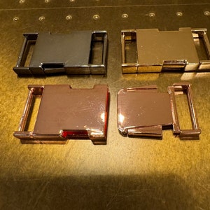 May include: Four metal clasps in different finishes: black, gold, rose gold, and rose gold. The clasps are all the same size and shape, and they have a simple, modern design.