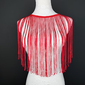 May include: A bright red fringe collar piece featuring a circular neckline with long, thin, hanging strands of red thread that drape downwards, creating a layered, linear texture across the chest area of the white display mannequin.
